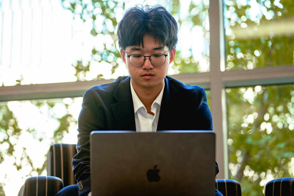 one person sitting in front of a window while on their laptop